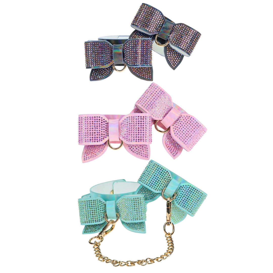 Adjustable ankle cuffs with rhinestone bows and gold chain leash, available in iridescent black, pink, and blue for stylish BDSM play.