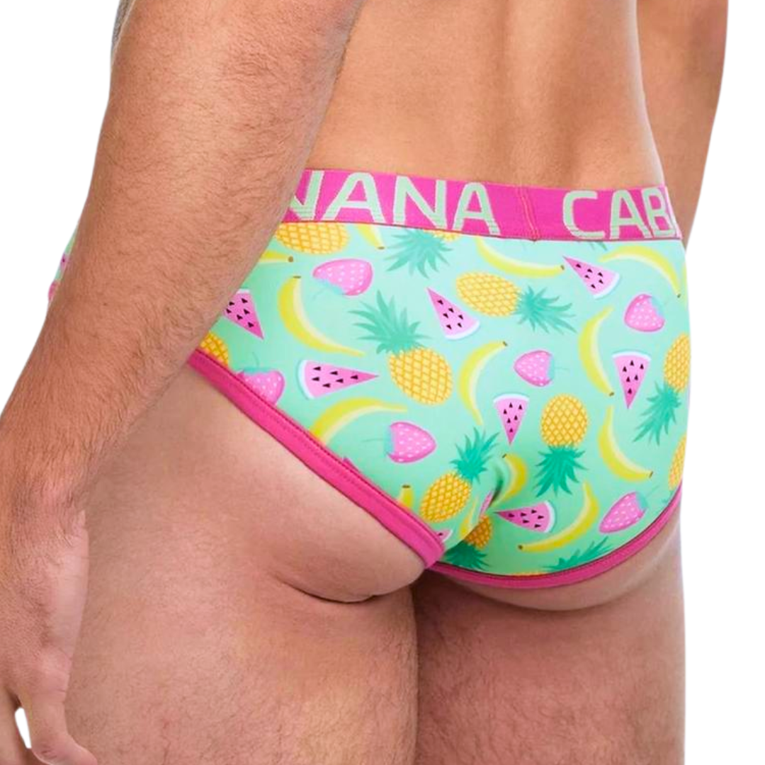 Brazilian bikini briefs with a tropical fruit salad print featuring bananas, pineapples, strawberries, and watermelon slices, and a bold pink Banana Cabana waistband.