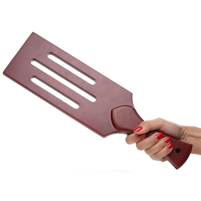 A dark brown wooden paddle with aerodynamic slots, designed for BDSM play, featuring a curved handle and durable construction for precision and impact.