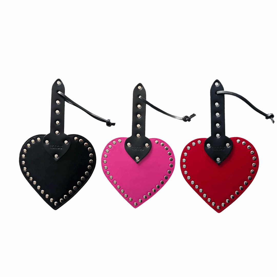 Heart-shaped leather spanking paddle with riveted studs, wrist strap, and genuine cowhide leather in pink, black, or red.
heart-shaped paddle, leather spanking paddle, genuine leather paddle, impact play paddle, heart impression paddle, luxury bondage paddle, studded spanking paddle, pink leather paddle, black leather paddle, red leather paddle, handcrafted BDSM paddle.